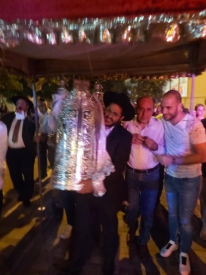 Community members walking together beneath a decorated canopy at an evening celebration